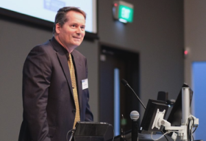 Dr Kevin Sowerby standing at a podium speaking.