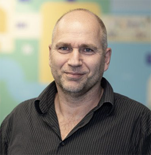 Klaas standing in front of a pastel green and blue coloured wall.